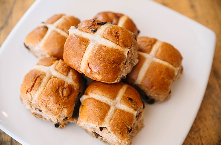 Six hot cross buns on a white, square plate.